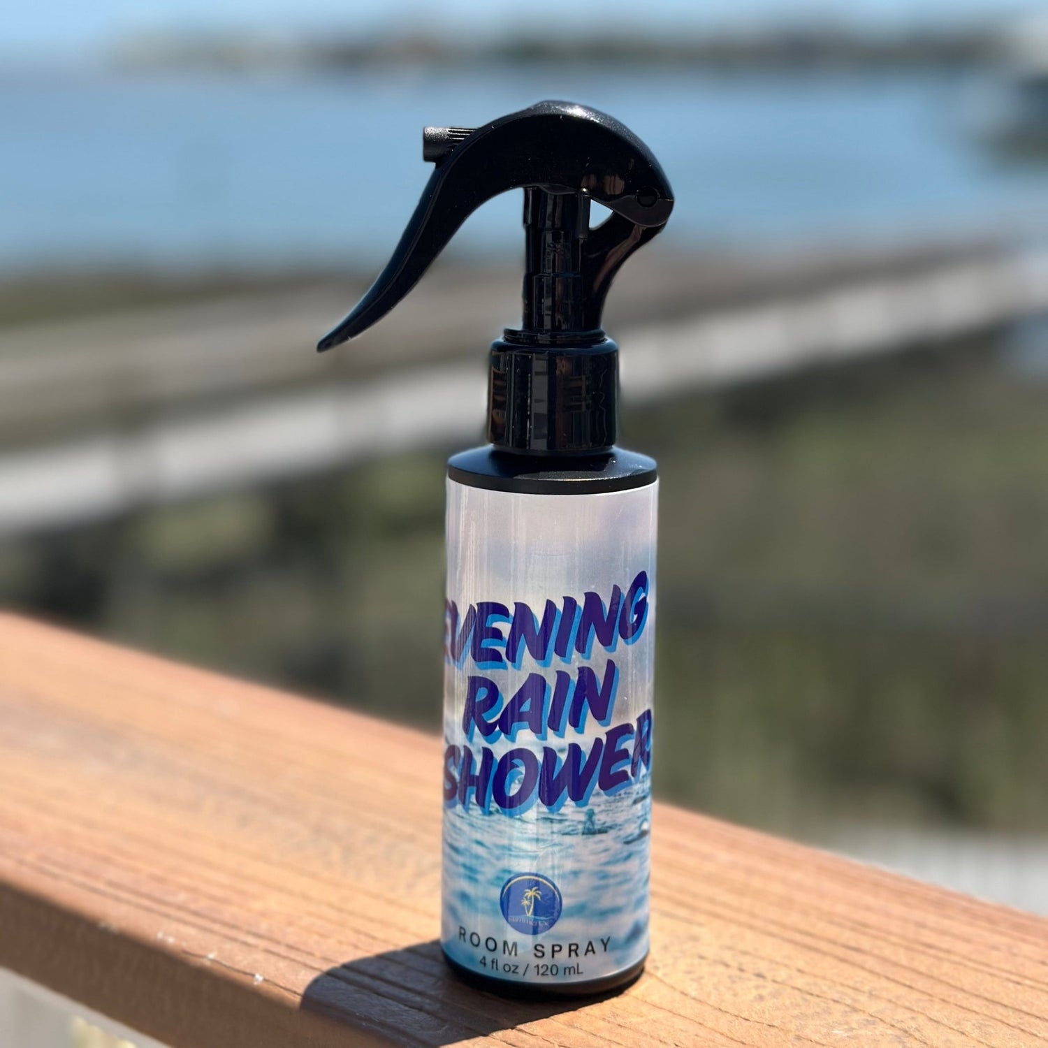 Bottle of 'Evening Rain Shower' spray on a wooden surface with a blurred natural background