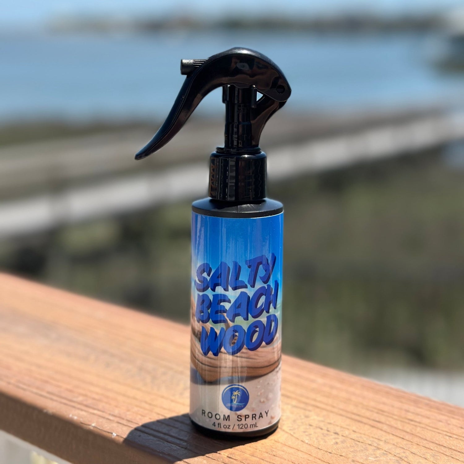 Salty Beach Wood room spray bottle on a wooden surface with a blurred natural background