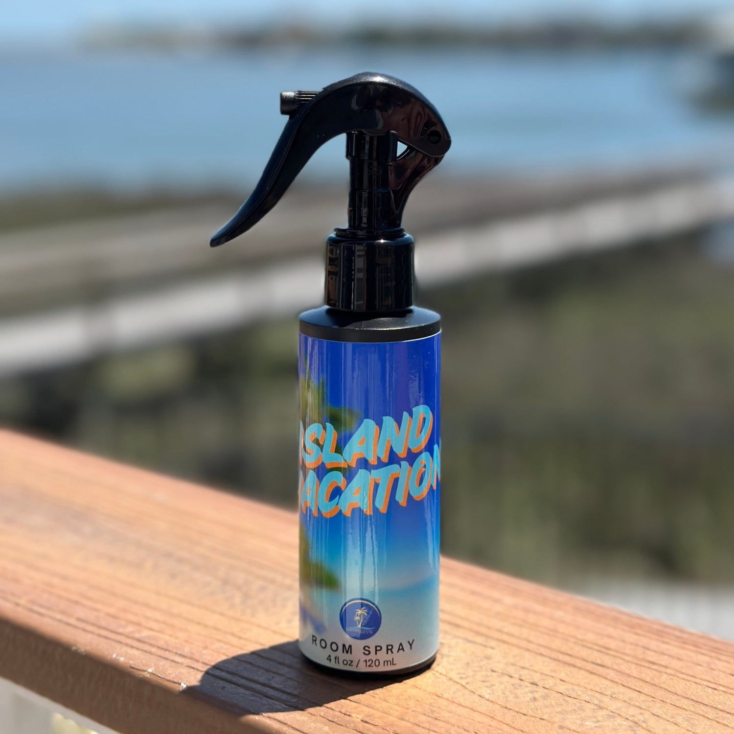 Room spray bottle labeled 'Island Vacation' on a wooden surface with a blurred outdoor background