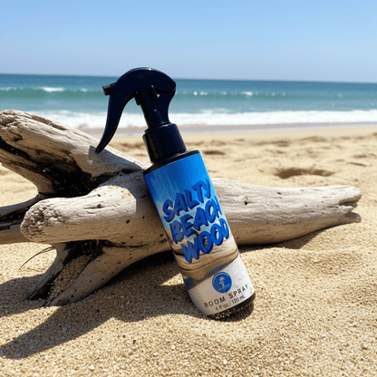 Room spray labeled 'Salty Beach Wood' on a beach with driftwood and ocean in the background