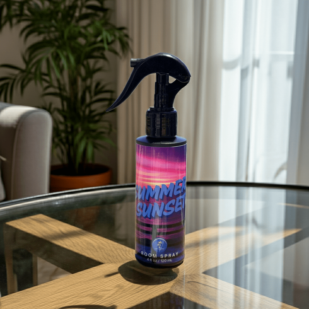 Room spray bottle labeled 'Summer Sunset' on a glass table with a plant and window in the background.