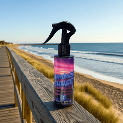 Bottle of 'Summer Sunset' room spray on a wooden railing with a beach background
